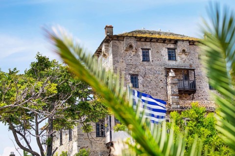 Ancient Ouranoupolis Tower on Athos peninsula in Halkidiki, flag of Greece. View through the palm
