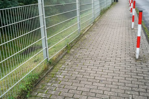 Sidewalk, metal fence on the left, red and white poles on the right