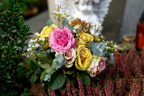Withered pastel-coloured roses lie on a grave, a white angel in the blurred background