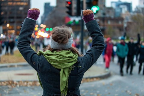 Young woman is raising her arms high while looking at the crowd during an ecological protest. Shot