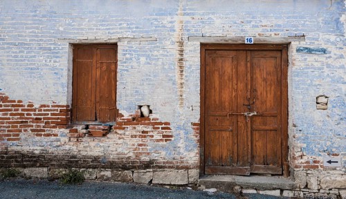 Exterior of an old village house with blue stoned wall and closed vitnage door and window