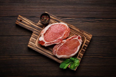 Cut raw meat pork steaks with seasonings on kitchen cutting board, rustic wooden background top
