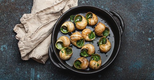 Escargots de Bourgogne Cooked Snails with Garlic Butter and Parsley in black cast iron pan on