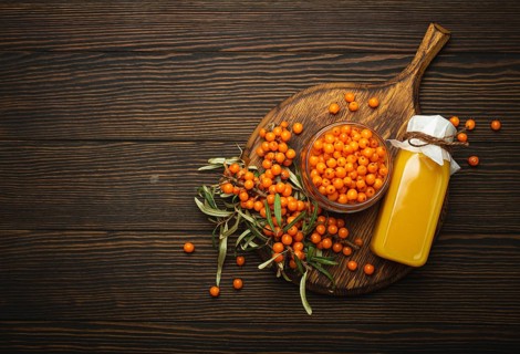 Sea buckthorn healthy drink in bottle, ripe berries in glass jar and branches with leaves top view