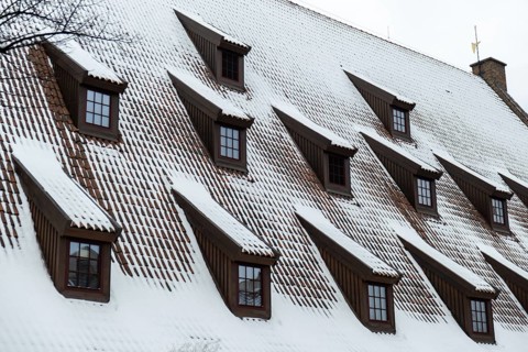 Snow falling on the roofs of the city. Snow-covered brown metal tiles roof of European house with