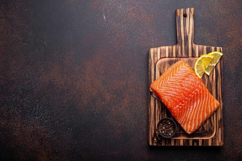 Fresh raw salmon fillet on wooden kitchen cutting board with seasonings and lemon top view on dark