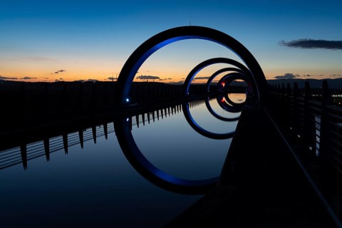 A view of the Falkirk Wheel at sunset with lights in different bright colors