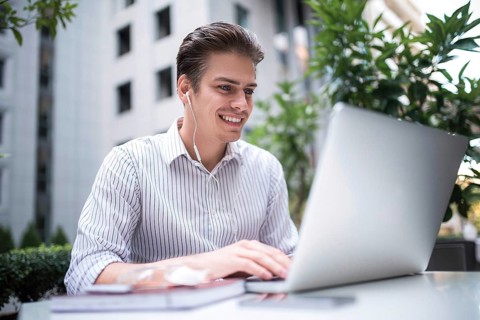 Happy handsome businessman looking at computer screen while typing something on laptop keyboard