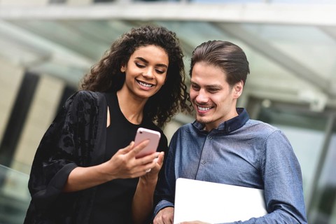 Business man and woman looking at smartphone together on building background in city outdoor