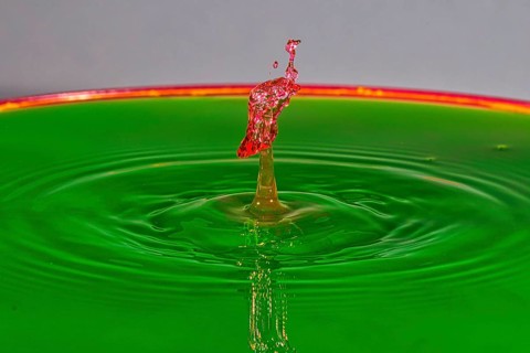 A red water drop rises dynamically on a green background, water drop, collision, high-speed
