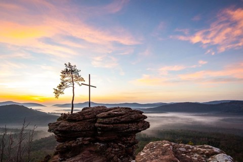Landscape shot of nature in the morning. Mist in the valley and a summit cross on a sandstone cliff