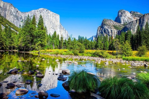Picturesque El Capitan and mountain peaks are reflected in the smooth water of the Merced River.