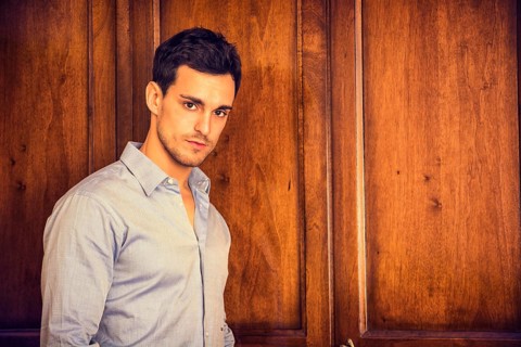 Sexy handsome young man standing wearing shirt in his bedroom against wooden wardrobe door