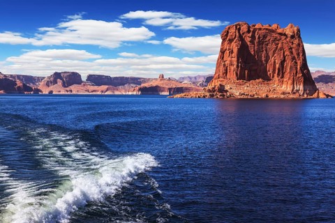 Foamy trace of a motor boat crosses the emerald waters. In the distance the coast of red sandstone.