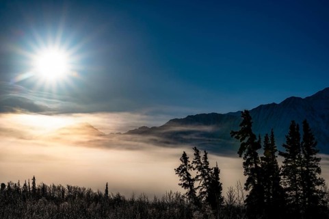 Sun over foggy, snow-covered landscape with mountain silhouette, Yukon, Canada, Kluane National