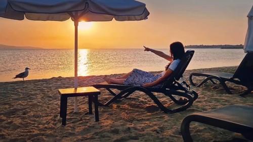 Young woman sitting on a sunbed at the beach pointing forefinger to the sunrise over the horizon.