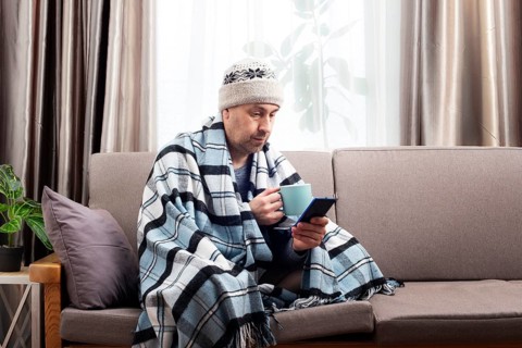 Middle age male model in hat and plaid hold coffee cup sitting on the sofa while using his