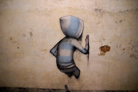 A lonely boy with a hood stands in front of a plain wall, creating a calm and minimalist