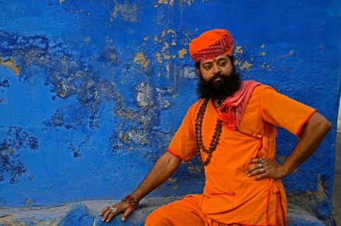 Priest saffron sitting against blue wall, Jodhpur, Rajasthan, India, Asia