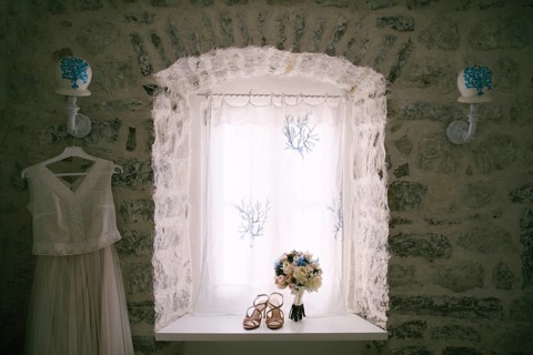 The bride's wedding dress by the window with the bride's bouquet and sandals on the windowsill.