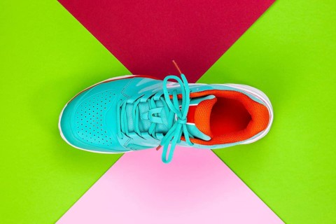 Red, cyan, white new tennis shoe in studio shot over green, pink, purple background. Directly from