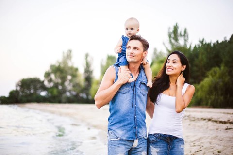 Beautiful young family on holiday with baby. The father holds the blonde girl in her arms, and the