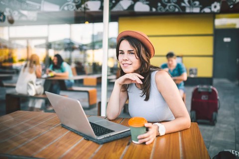 Beautiful young caucasian woman sitting on a terrace in a cafe in summer at a wooden table in a hat