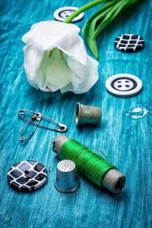 One white tulip and buttons with threads on turquoise wooden background