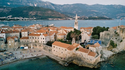 Stone fortress walls of the old town near the high bell tower. Budva, Montenegro. Drone.