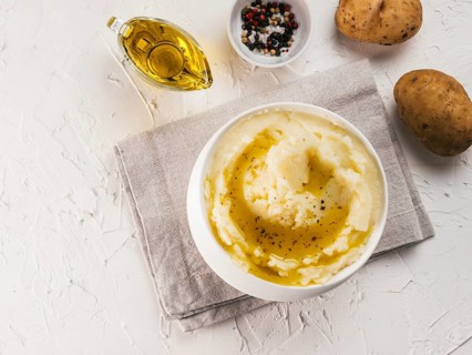Mashed potatoes in white bowl with cloth napkin, pepper and olive oil on textured concrete white