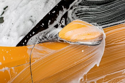 Detail on strokes left by brush in shampoo and foam, front mirror of a car washed in carwash