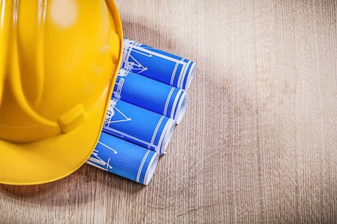 Wooden board with blue rolled up construction drawings building helmet