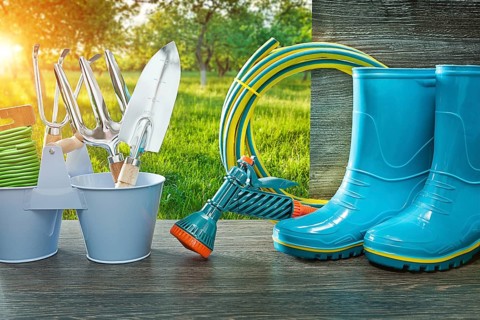 Gardening tools blue rubber rain boots hose sprayer gun spade and fork on vintage table in spring