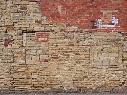 An old exterior wall with an irregular patched and repaired brick and stone surface