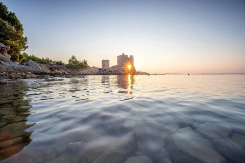 Castle ruins at dawn. Bay on the Mediterranean Sea with calm water at sunrise. Reflection of the