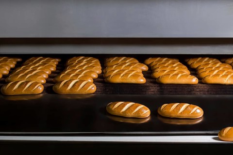 Baguettes baking in industrial oven. Loaves of bread at production line. Food factory