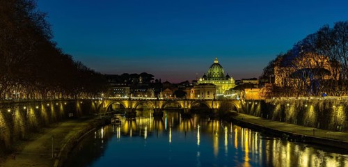 A picture of the St. Angelo Bridge, the St. Peter's Basilica and the Tiber river at night