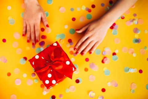 From above of anonymous female with wrapped present decorated with red ribbon and placed on yellow