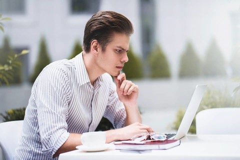 Smart attitude. Positive handsome man using a laptop and sitting in the cafe while surfing the