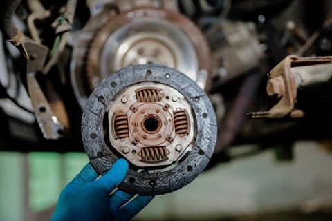 Clutch plate shown by a hand in blue glove in an automotive repair setting
