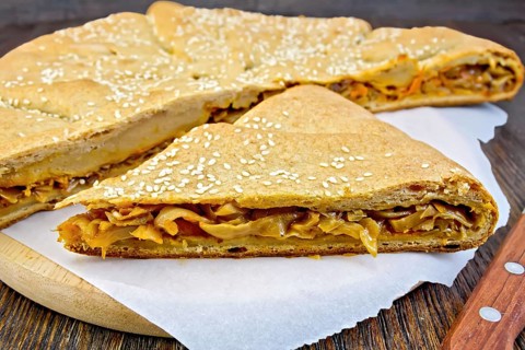 Pie with cabbage and sesame seeds with fresh rye dough knife on a wooden boards background