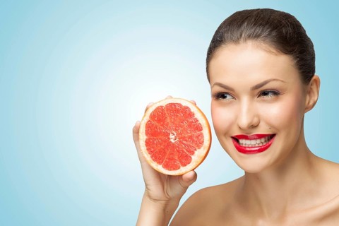 A creative portrait of a beautiful girl holding a red grapefruit sexually under her chin
