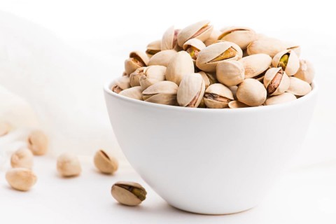 Bowl of roasted pistachios on a white background