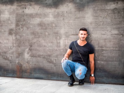 Handsome young man standing against concrete wall, looking at camera, wearing black t-shirt and