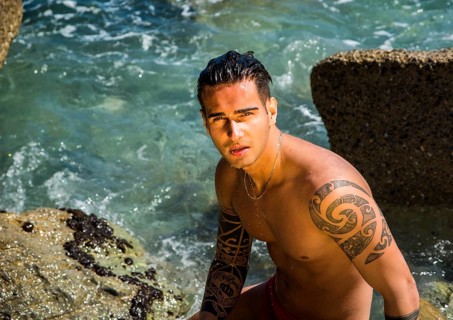Attractive young shirtless athletic man standing in water by sea or ocean shore, wearing shorts,