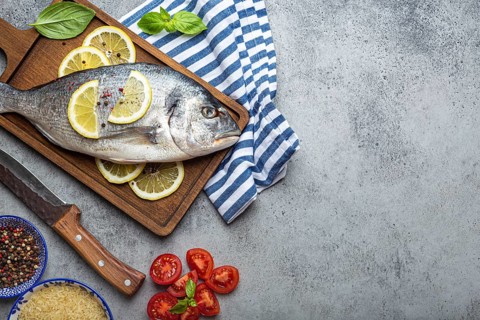 Raw fish dorado with ingredients lemon, fresh basil, cut cherry tomatoes, uncooked rice on wooden