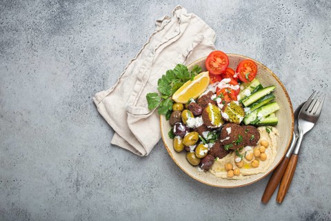 Falafel salad bowl with hummus, vegetables, olives, herbs and yogurt sauce. Vegan lunch plate top