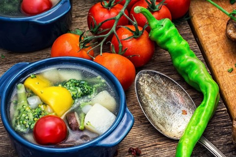 Traditional soup of fresh vegetables in blue pot on wooden background.Photo tinted