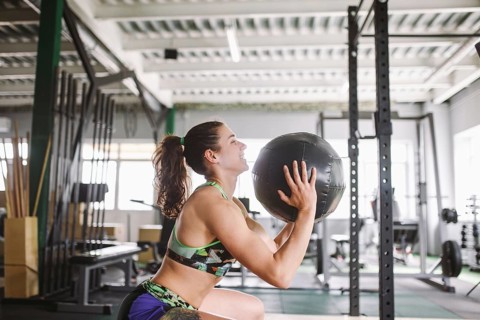 Healthy girl doing exercises on muscles of legs and hands with the ball in hands in the gym