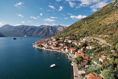 Boat is moored in the bay near the winding shore of Perast with a view of the bell tower.